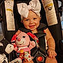 baby, infant, child, car_seat, toy, plush_toy, bow_headband, smiling, happy, indoor, person, clothing, seatbelt, foot, hand, face, head, sitting, cute, playful