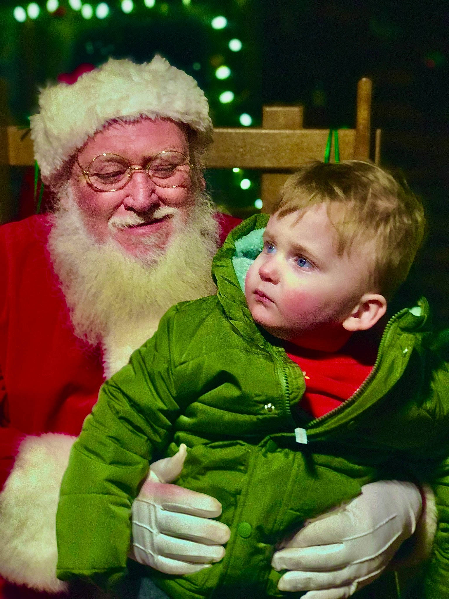 Lawton is registered to the contest to win money with this photo: baby, beard, christmas, christmas_eve, event, fictional_character, fun, glasses, green, hair, happy, hat, headwear, holiday, human_body, lap, organ, person, santa_claus, smile