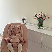 Vira is registered to the contest to win money with this photo: baby, pink, baby_seat, toy, flower_vase, pink_flowers, dresser, carpet, headband, baby_clothing, smile, indoor, infant, portrait, person, furniture, room, decor, photography, happy