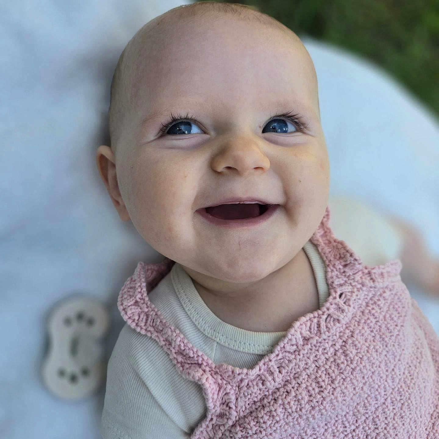Eléanore participe au concours pour gagner de l'argent avec cette photo : baby, background_blur, blanket, blue_eyes, child, closeup, cute, face, happy, infant, knitted, natural_light, outdoor, person, pink_clothing, portrait, skin, smiling, soft_texture, toddler