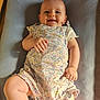 baby, child, clothing, cushion, cute, face, floral_pattern, happy, indoors, infant, lying_down, natural_light, person, portrait, romper, skin, small_feet, small_hands, smile, soft_texture