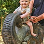 adult, arm, baby, child, cute, greenery, happy, nature, outdoor, park, person, playful, portrait, sculpture, smiling, summer, sunlight, tattoo, toy, wooden_elephant