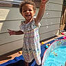 backyard, bucket, child, curly_hair, daytime, dress, fun, happy, outdoor, patio, person, playing, pool, smiling, splash, summer, sunlight, toddler, toy, water