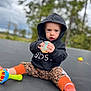 toddler, child, hoodie, black_clothing, ball, toy, trampoline, outdoor, nature, trees, sitting, leopard_print_pants, orange_socks, cute, face, expression, person, young_child, casual_clothing, playtime