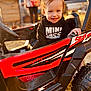toddler, child, smiling, toy_car, hoodie, outdoor, sunlight, vehicle, red, black, happy, cute, person, portrait, daylight, small_child, play, fun, expression, casual