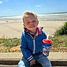 Owen a rejoint le concours — aidez-le/la à gagner de superbes lots ! child, boy, smiling, blue_jacket, jeans, beach, ocean, sky, sunny, grass, stone_wall, cup, straw, paw_patrol, outdoor, happy, portrait, sitting, daylight, casual_clothing