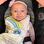 baby, infant, car_seat, headband, flower, bib, pacifier, blanket, drool, pink_clothing, child, cute, portrait, indoors, seatbelt, happy, face, blue_eyes, soft_lighting, cozy