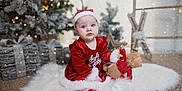Everleigh joined the competition — help win amazing prizes! baby, child, christmas, holiday, santa_hat, red_clothing, teddy_bear, white_rug, decorations, tree, gift_boxes, snow, festive, indoors, cute, portrait, smiling, seasonal, soft_lighting, cozy
