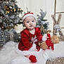 baby, child, christmas, holiday, santa_hat, red_clothing, teddy_bear, white_rug, decorations, tree, gift_boxes, snow, festive, indoors, cute, portrait, smiling, seasonal, soft_lighting, cozy