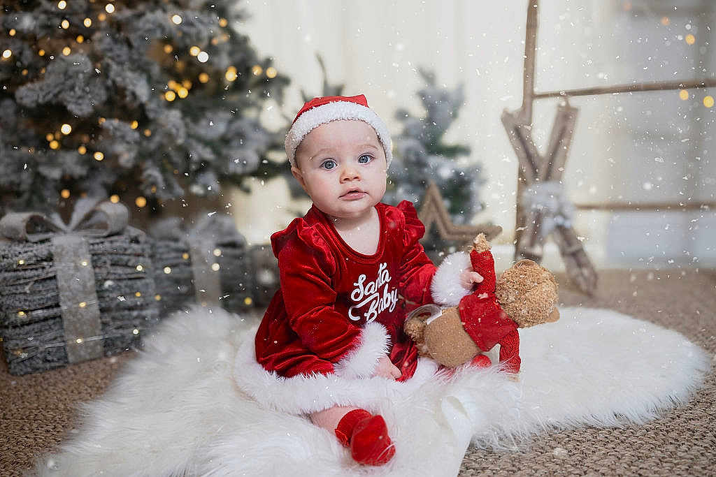 Everleigh joined the competition — help win amazing prizes! baby, child, christmas, holiday, santa_hat, red_clothing, teddy_bear, white_rug, decorations, tree, gift_boxes, snow, festive, indoors, cute, portrait, smiling, seasonal, soft_lighting, cozy