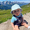baby, child, infant, mountains, alps, snowy_peaks, landscape, outdoors, hiking, travel, sun_hat, overalls, blue_shirt, sitting, rock, wildflowers, meadow, sunlight, portrait, scenic_view