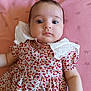 baby, infant, child, dress, floral_pattern, white_collar, pink_blanket, lying_down, portrait, cute, skin, face, eyes, arms, buttoned_dress, soft_texture, indoors, closeup, adorable, calm