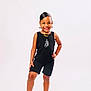 child, smile, posing, black_outfit, earrings, necklace, shorts, socks, standing, white_background, happy, fashion, portrait, studio, cute, person, confident, accessories, young, feet
