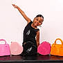 child, girl, smile, pose, handbags, pink, orange, black, heart_shaped, studio, portrait, fashion, accessories, earrings, black_dress, bench, happy, young, cute, colorful