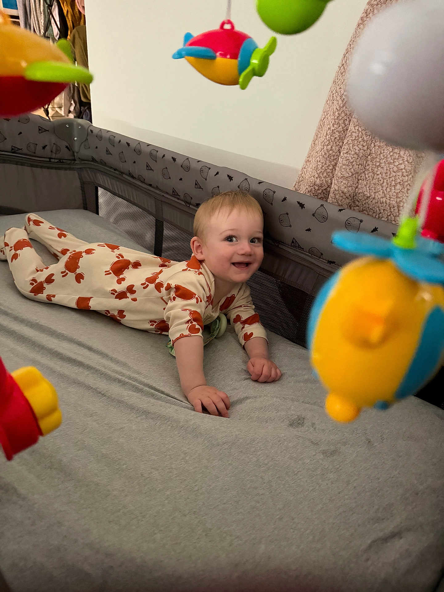 Lucas joined the competition — help win amazing prizes! baby, crib, pajamas, toy, smiling, tummy_time, indoor, child, hanging_toy, blanket, clothing, face, person, bed, play, happy, infant, room, colorful, cute