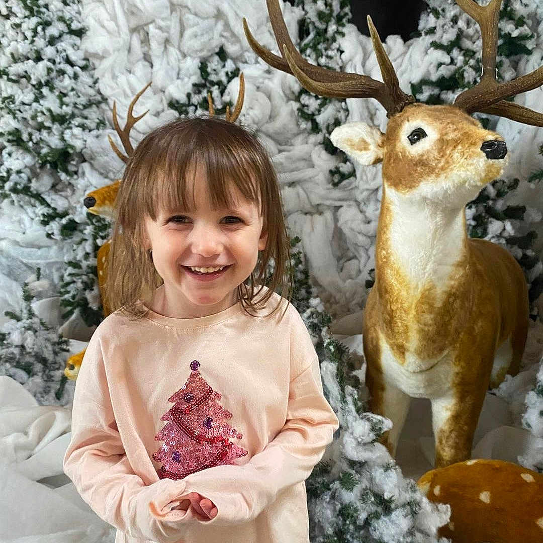 Naya participe au concours pour gagner de l'argent avec cette photo : antlers, background, child, christmas_tree_design, cute, decoration, deer_statue, festive, happy, holiday, indoor_scene, person, pink_shirt, playful, portrait, seasonal, smiling, snow, snowy_trees, winter