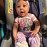 baby, car_seat, infant, purple_clothing, headband, socks, cute, surprised_expression, child, seatbelt, warning_label, indoor, person, apparel, toddler, child_seat, plush, pink, cartoon_characters, smile