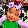 Emerald is registered to the contest to win money with this photo: baby, woman, glasses, purple_bow, smile, store_aisle, shelves, products, clothing, patterned_jacket, green_baby_carrier, face, headwear, person, indoor, shopping, happy, closeup, holding, infant