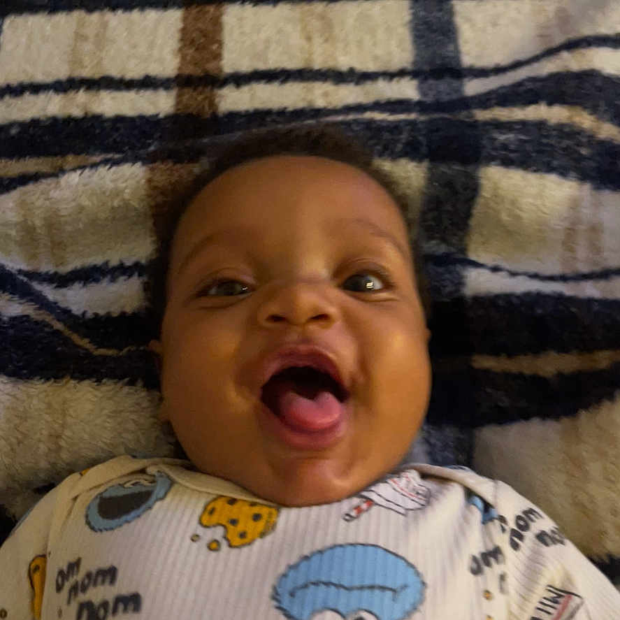 Kairo joined the competition — help win amazing prizes! baby, infant, smiling, happy, onesie, cartoon, blanket, striped, face, expression, mouth_open, cute, child, lying_down, indoors, person, young, playful, clothing, pattern