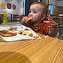 toddler, child, burger, food, table, restaurant, fast_food, fries, eating, brown_hair, curious, indoor, clothing, high_chair, paper_wrap, hand, face, mouth, seat, casual