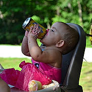 Serenity is registered to the contest to win money with this photo: toddler, child, pink_clothing, high_chair, cupcake, crumbs, tissue_paper, drink_can, messy_hands, balloon, outdoor, sunlight, greenery, person, summer, party, celebration, face, mouth, hair