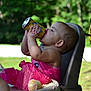 toddler, child, pink_clothing, high_chair, cupcake, crumbs, tissue_paper, drink_can, messy_hands, balloon, outdoor, sunlight, greenery, person, summer, party, celebration, face, mouth, hair