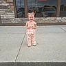 building, car, casual, child, clothing, concrete, daylight, flower_pattern, happy, outdoor, person, pigtails, portrait, reflection, sidewalk, smiling, stone_wall, toddler, urban, window