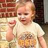 brick_wall, casual_clothing, child, curious, daylight, gesture, girl, leopard_print, outdoor, person, pigtails, pink_bows, portrait, sidewalk, smile, stone_wall, text, toddler, tshirt, young_child