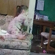 Hope is registered to the contest to win money with this photo: carpet, chair, child, clutter, couch, cup, floor, footwear, furniture, hair_tied, home, indoors, living_room, pajamas, paper, person, side_view, table, toy, wood_panel_wall