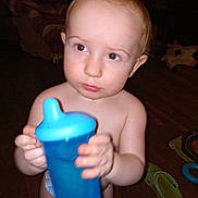 Duwane joined the competition — help win amazing prizes! toddler, child, blue_sippy_cup, indoor, floor, toy, slippers, bare_chest, diaper, curious, young_child, person, holding, looking_away, home, wooden_floor, plastic_cup, expression, standing, baby