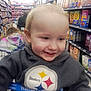 toddler, child, smile, shopping_cart, grocery_store, cereal_aisle, hoodie, sweatshirt, steelers_logo, walmart_strap, blond_hair, closeup, candid, happy, aisle_shelves, retail, shopping, family_shopping, baby_face, indoor_lighting