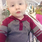 Duwane is registered to the contest to win money with this photo: child, toddler, face, person, clothing, hoodie, shopping_cart, store, indoor, sitting, baby, portrait, young_child, casual_wear, looking_at_camera, aisle, retail, bright_lighting, curious_expression, shopping