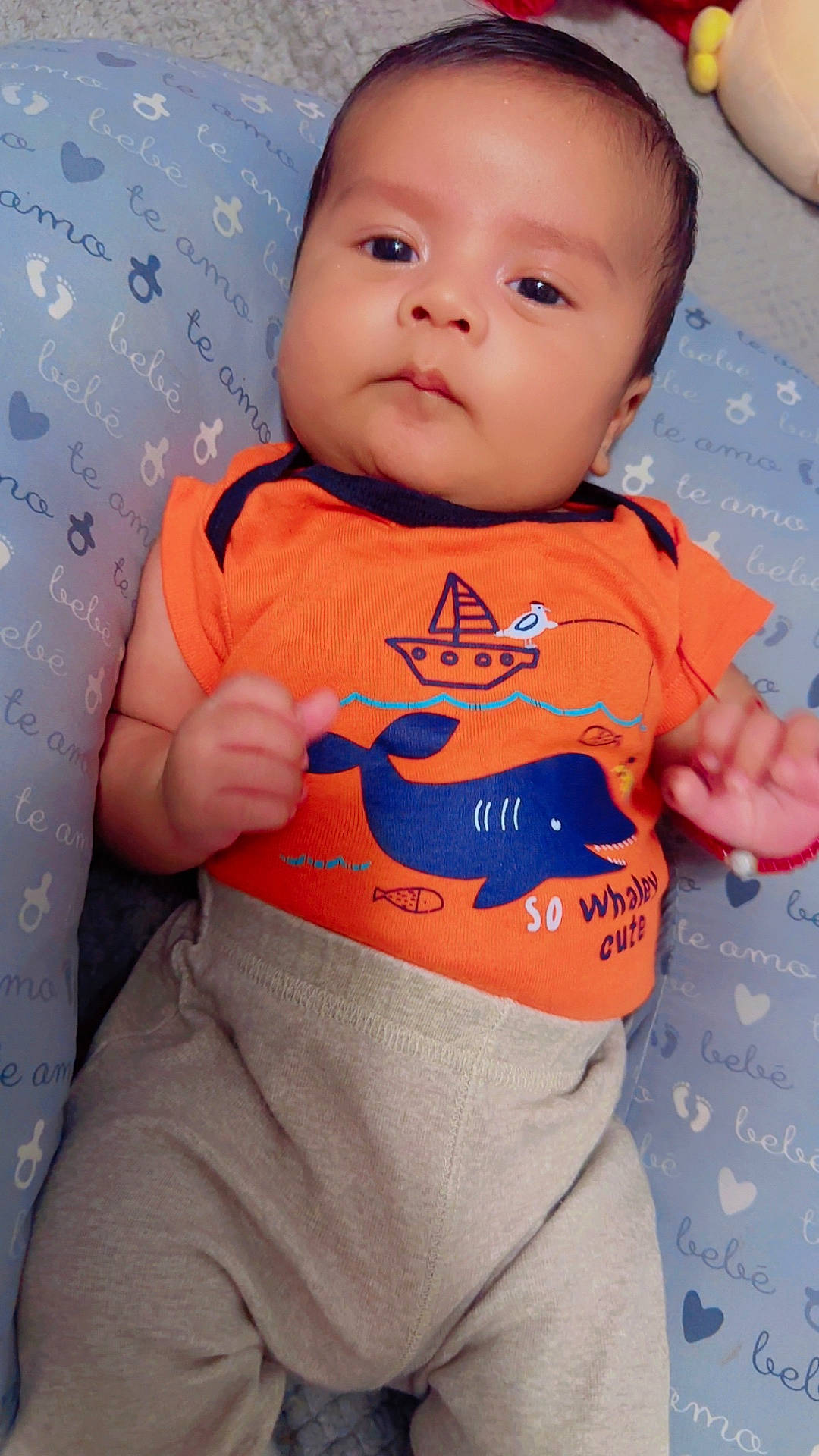 Jaziel is registered to the contest to win money with this photo: baby, child, clothing, cute, expression, eyes, face, hands, head, indoors, infant, lying_down, orange_shirt, pattern, person, pillow, portrait, skin, toddler, whale_design