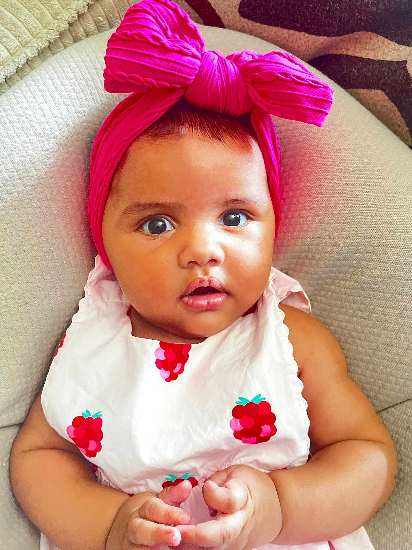 Luna a rejoint le concours — aidez-le/la à gagner de superbes lots ! baby, child, headband, pink, bow, dress, raspberry, fruit_print, cushion, closeup, portrait, curious, hands, infant, indoor, cute, adorable, skin, face, seated