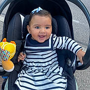 Luna a rejoint le concours — aidez-le/la à gagner de superbes lots ! baby, black_car_seat, blue_bow, car_seat, child, cute, face, hand, happy, infant, outdoor, pavement, person, plush_toy, purple_tights, road, seatbelt, smiling, striped_dress, toy