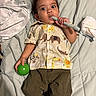 toddler, child, baby, bed, blanket, green_ball, teething_toy, animal_print_shirt, pants, diaper, lying_down, indoors, cute, wide_eyes, handheld_object, soft_surface, casual_clothing, portrait, infant, playful
