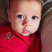 Luciano is registered to the contest to win money with this photo: baby, blue_eyes, child, closeup, couch, cute, face, indoors, infant, looking, newborn, onesie, person, pillow, portrait, red_clothing, resting, skin, soft_lighting, young_child