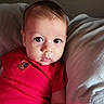 Luciano is registered to the contest to win money with this photo: baby, child, closeup, comfortable, cute, expression, eyes, face, head, indoors, infant, looking_at_camera, person, pillow, portrait, red_onesie, skin, sleepwear, soft_light, young_child