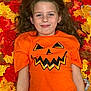 child, girl, autumn_leaves, orange_shirt, jack_o_lantern, smiling, long_hair, fall, seasonal, portrait, happy, casual_clothing, outdoor, nature, colorful, leaf_background, festive, young_person, holiday, playful