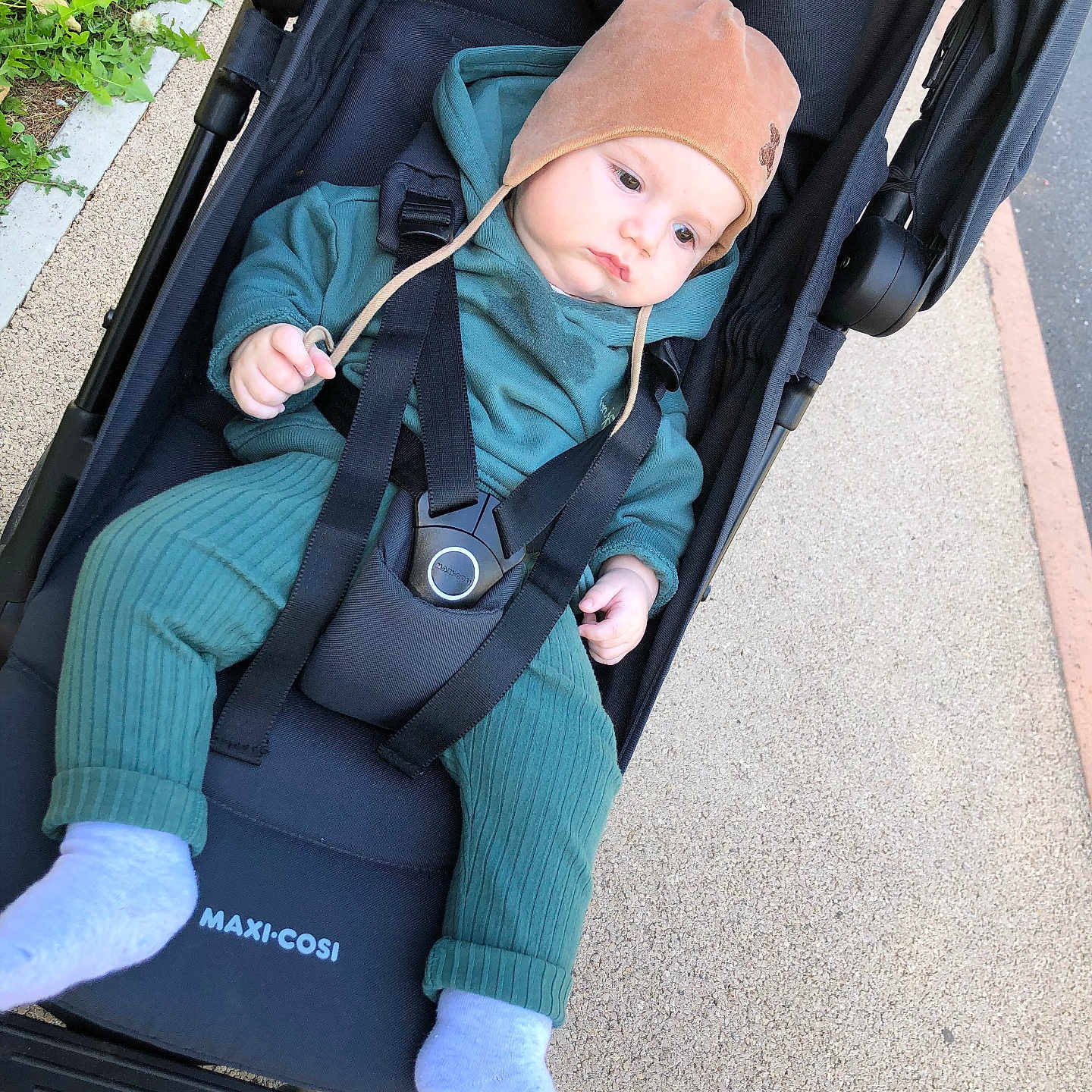 Alex a rejoint le concours — aidez-le/la à gagner de superbes lots ! baby, baby_hat, baby_sock, baby_wear, black_stroller, casual, child, clothing, daylight, footwear, green_outfit, hat, infant, outdoor, pavement, person, relaxed, seat_belt, sidewalk, stroller