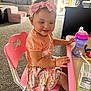 Zarra is registered to the contest to win money with this photo: toddler, girl, pink_bow, headband, pink_chair, table, sippy_cup, juice_box, carpet, living_room, couch, toy, smiling, child, indoor, casual_clothing, floral_skirt, playful, happy, furniture