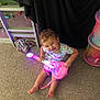 Zarra joined the competition — help win amazing prizes! child, toddler, toy_guitar, glowing, carpet, smiling, indoor, playroom, colorful, toy, barefoot, clothing, sitting, fun, happy, person, furniture, black_curtain, storage_bin, floor