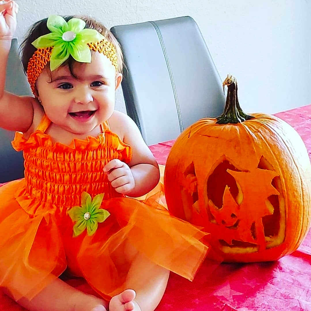 Mia joined the competition — help win amazing prizes! baby, clothing, costume, face, festival, food, halloween, happy, head, jack_o_lantern, person, photography, plant, portrait, pottedplant, produce, sitting, squash, vegetable