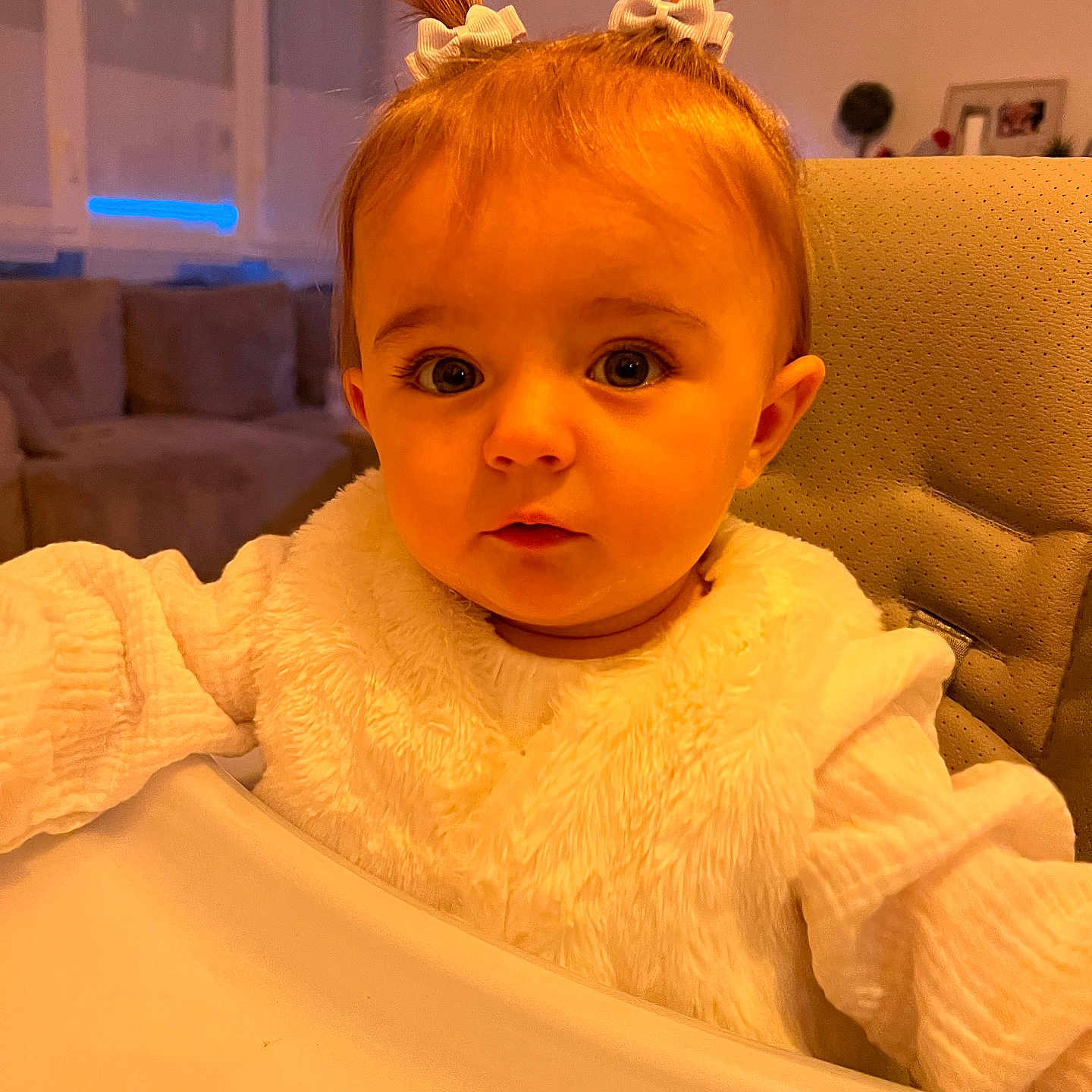 Romy a rejoint le concours — aidez-le/la à gagner de superbes lots ! baby, child, cozy, curious, cute, face, high_chair, indoor, infant, living_room, person, pigtails, portrait, seated, sofa, soft_lighting, white_bow, white_clothing, window, young_child