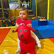 Romy participe au concours pour gagner de l'argent avec cette photo : toddler, child, indoor_play_area, red_toy, inflatable, ball_pit, colorful, playground, soft_mats, yellow_mat, blue_cushion, red_shirt, curious_expression, mesh_enclosure, play_equipment, socks, toy_dog, young_child, fun, leisure