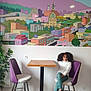 Naï participe au concours pour gagner de l'argent avec cette photo : child, girl, curly_hair, purple_chair, table, indoor, mural, wall_art, cityscape, springfield, casual, playful, tongue_out, green_pants, white_sweater, black_shoes, wooden_table, modern_chair, plant, relaxed