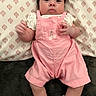 Analeia is registered to the contest to win money with this photo: baby, infant, pink_overalls, cherry_emblem, white_socks, pillow, patterned_pillow, dark_blanket, clothing, child, person, face, cute, indoors, laying_down, looking_at_camera, skin, head, hands, feet
