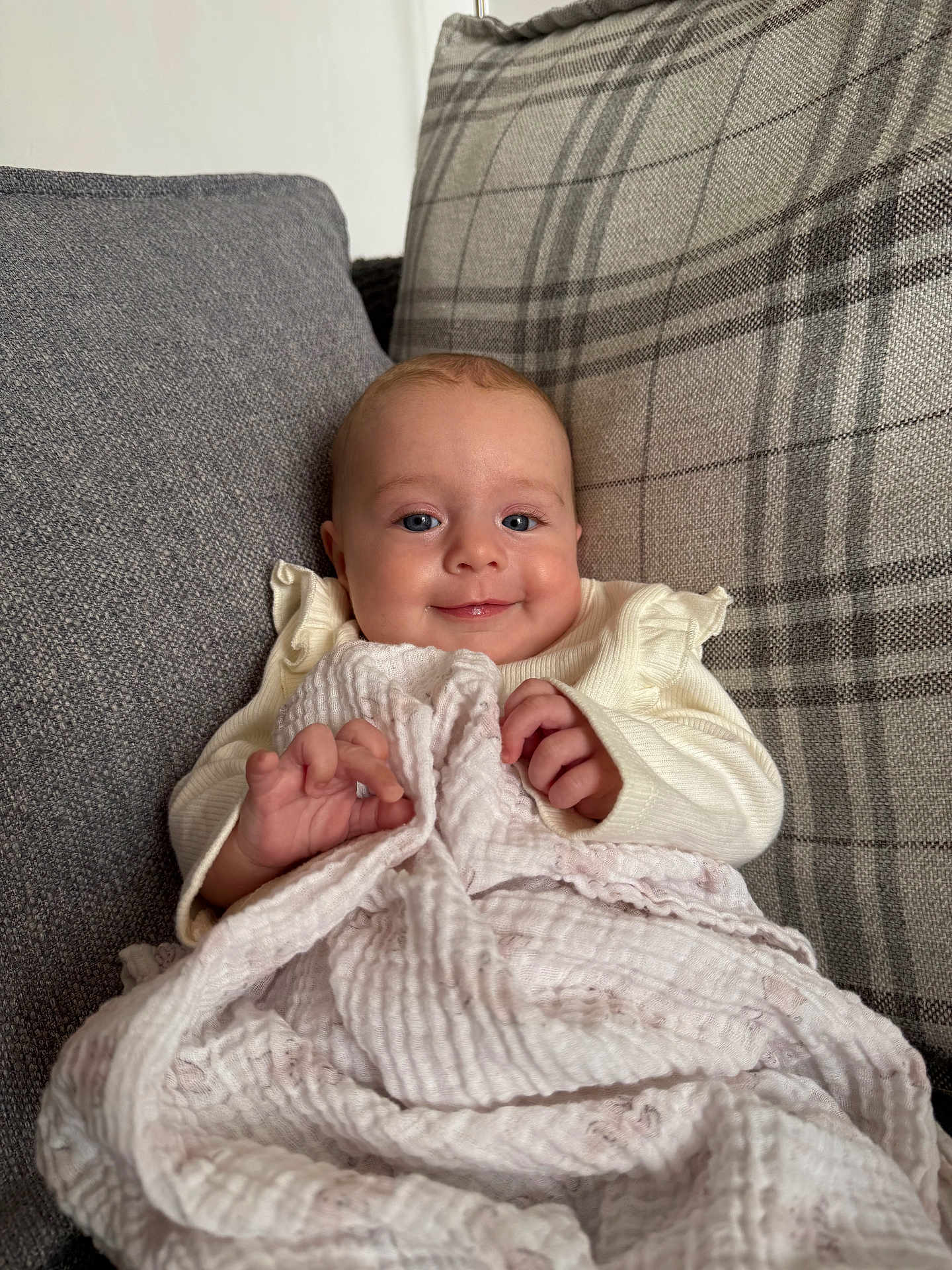Esmé joined the competition — help win amazing prizes! baby, smiling, blanket, cushion, plaid, gray, cozy, infant, child, portrait, indoor, soft_texture, clothing, cute, hands, face, comfort, seated, happy, young