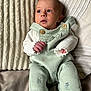 baby, infant, pillow, blanket, clothing, socks, face, person, portrait, indoor, soft_texture, curious, cute, newborn, seated, hands, head, light, fabric, cozy