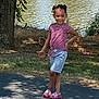 child, girl, smiling, pose, outdoor, lake, tree, grass, sidewalk, sandals, shorts, striped_shirt, sunlight, shadow, nature, happy, summer, playful, casual_clothing, daytime